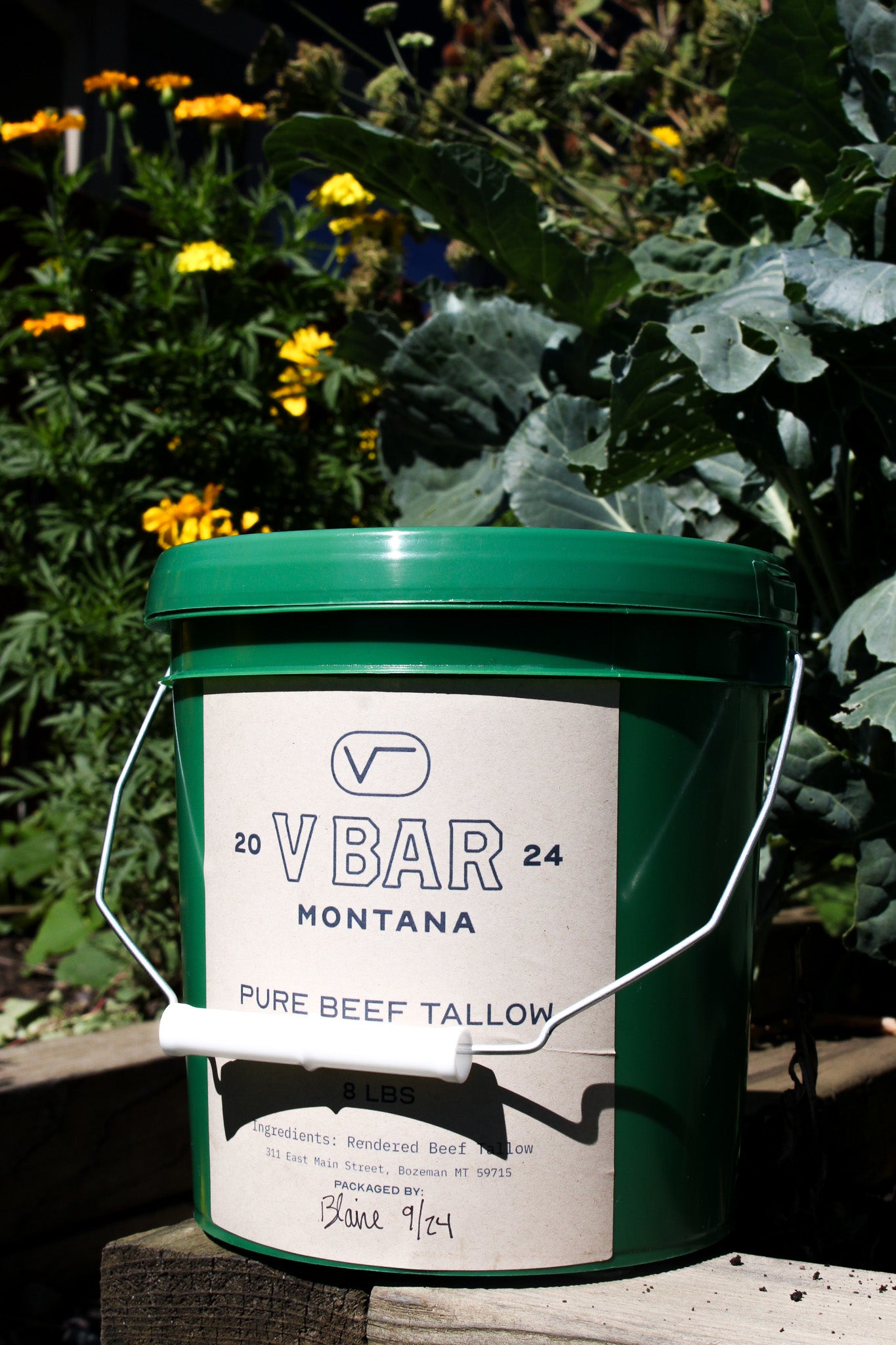Green bucket of pure beef tallow by flowers