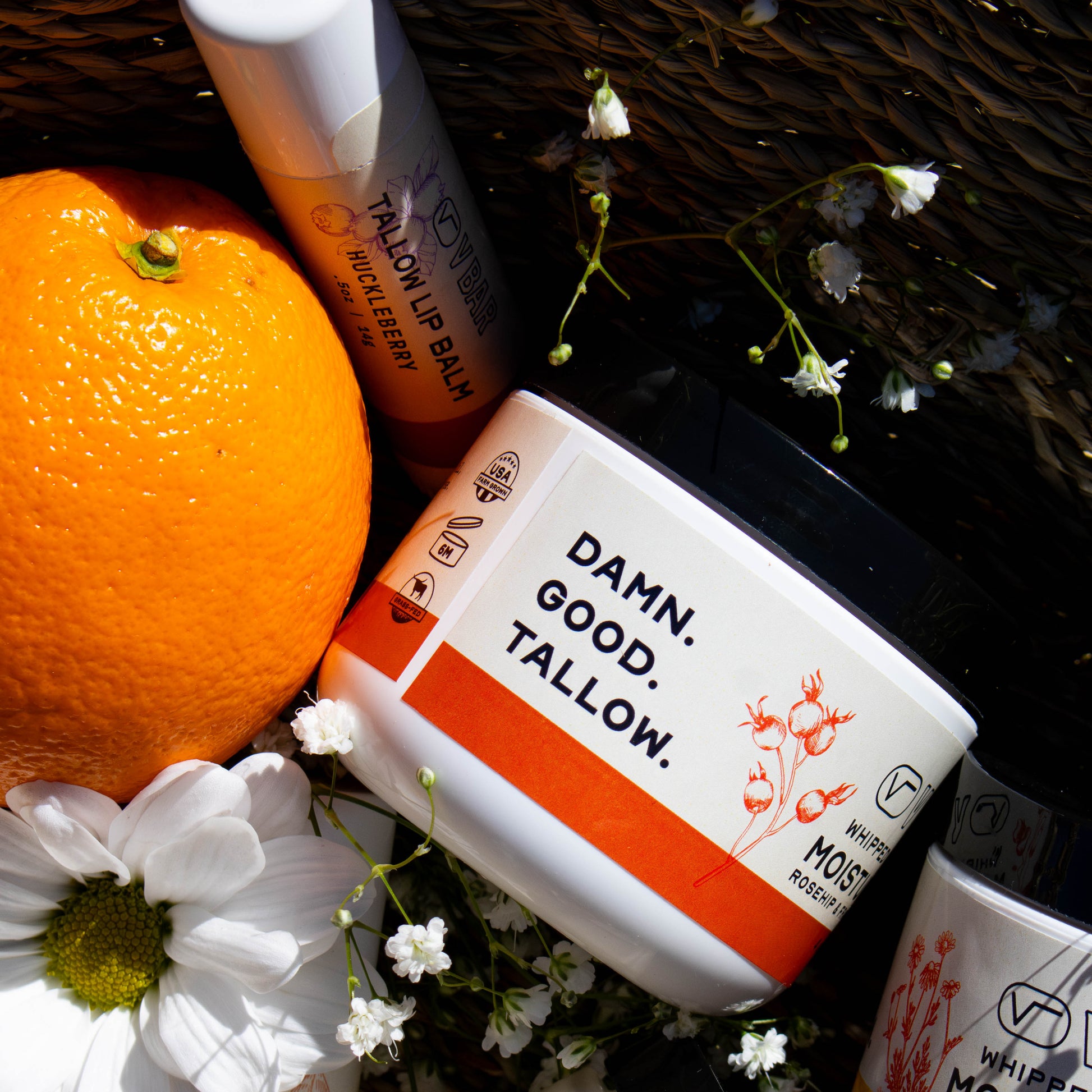 Whipped tallow moisturizer made from grass-fed beef suet sourced from Montana ranches laying in a basket surrounded by flowers and other products