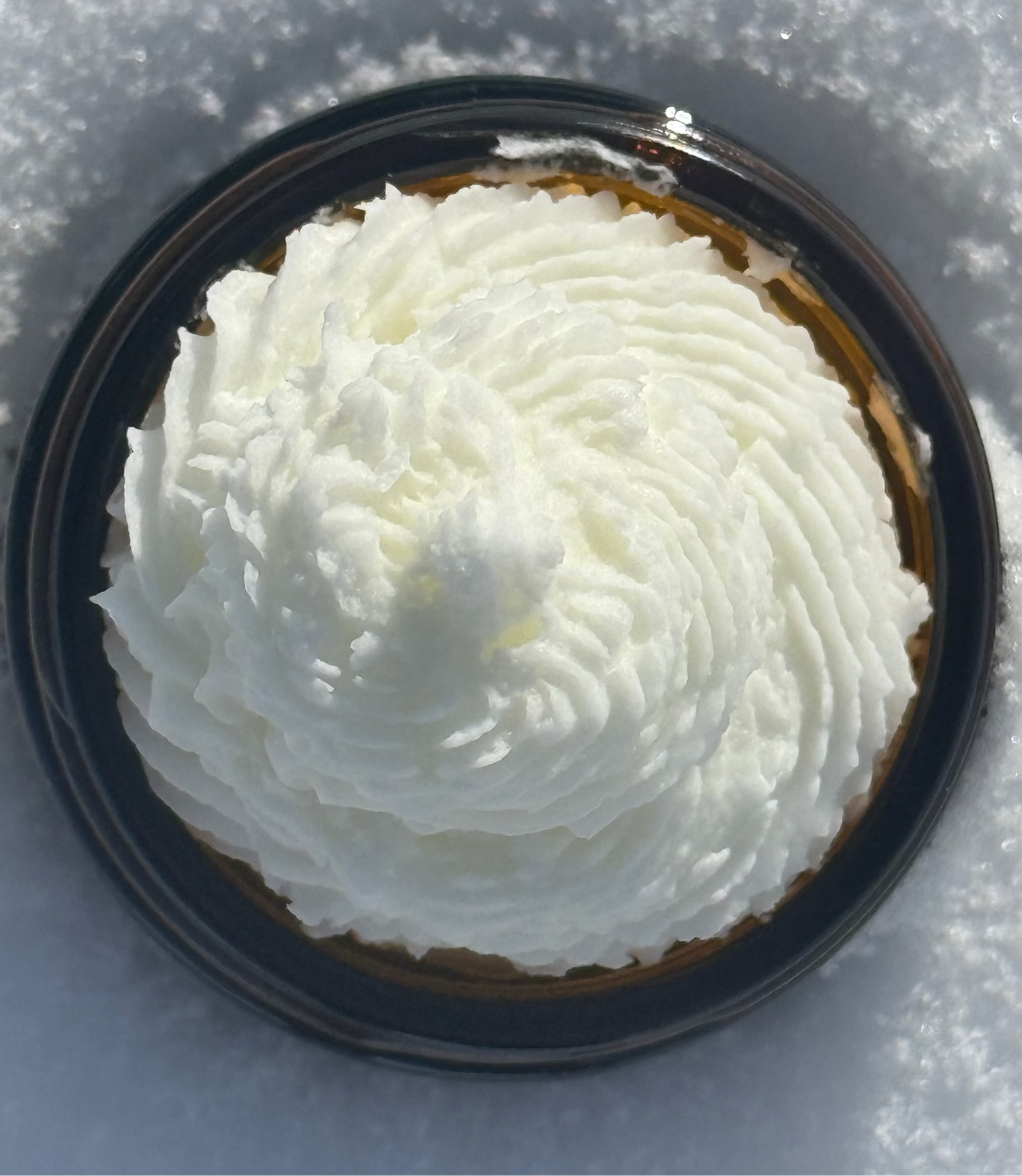 A jar of Beef Tallow moisturizer with a white, whipped texture, placed on a surface with a snowy background.